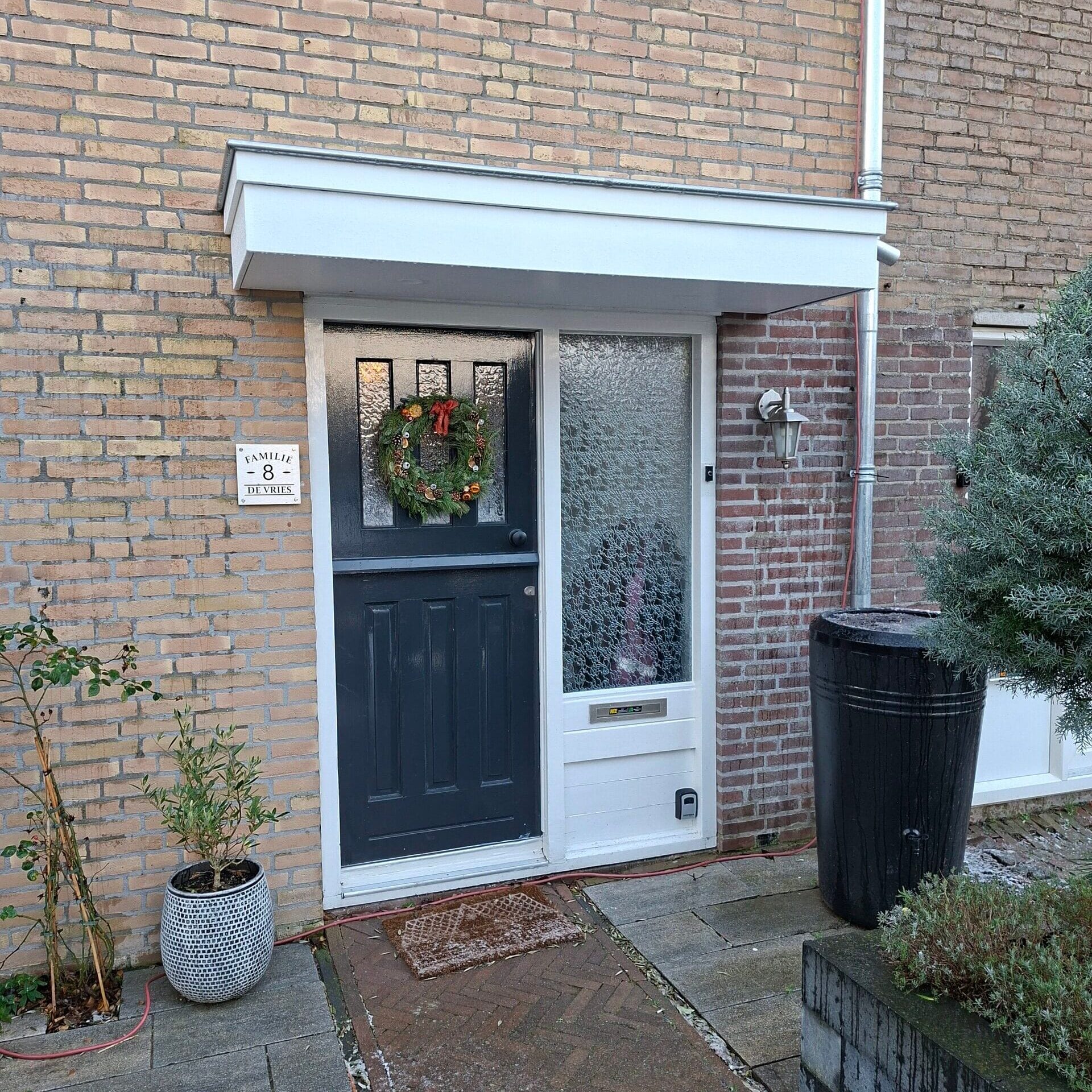 Nieuwe zwarte voordeur met deurluifel en kerstkrans, in een bakstenen gevel