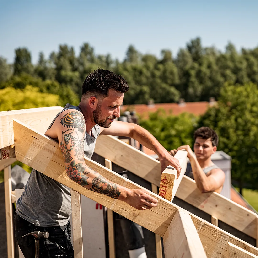 Gerben en Siebe de Vries plaatsen samen een houten gording op een dakconstructie