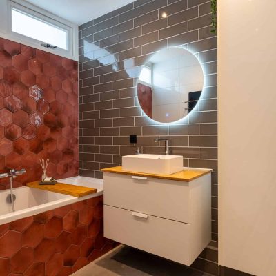 Badkamer met rode zeshoekige tegels rond het bad en een zwevend wastafelmeubel