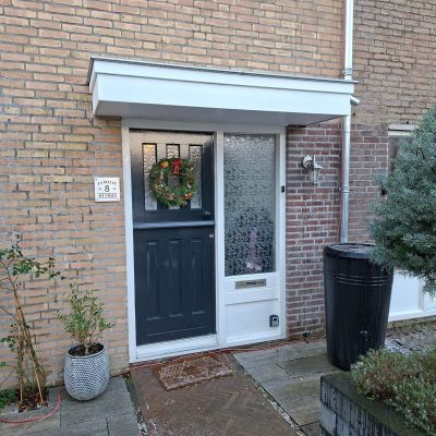 Nieuwe zwarte voordeur met deurluifel en kerstkrans, in een bakstenen gevel