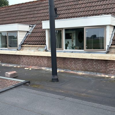 Twee dakkapellen op een pannendak tijdens de renovatie, met nieuwe dakpannen klaarliggend
