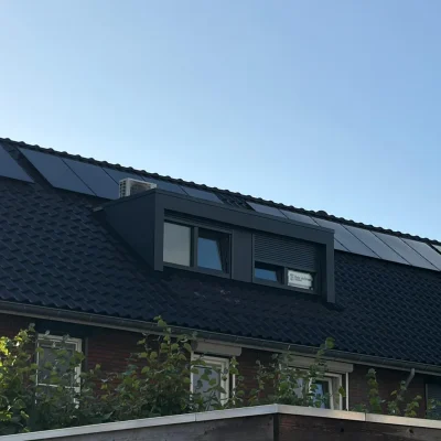 Zijaanzicht van een woning met een nieuw geplaatste dakkapel met donkere gevelbekleding en vier ramen, waarvan er een deels schuilgaat achter een naambordje