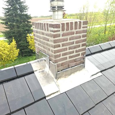 Bakstenen schoorsteen met nieuwe zinken voetloodaansluiting op het leien dak