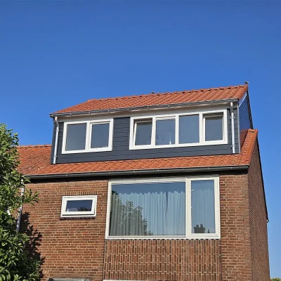 Zijaanzicht van een rijtjeswoning met een gerealiseerde nokverhoging met antracietkleurige gevelbekleding