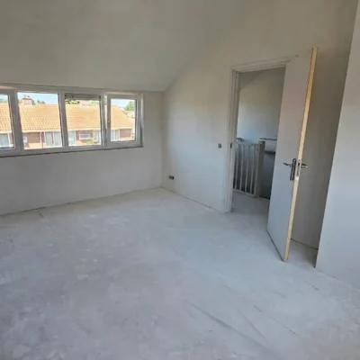 Kale, gestucte kamer onder het nieuwe schuine dak na de nokverhoging, met een raam en een deur naar het balkon