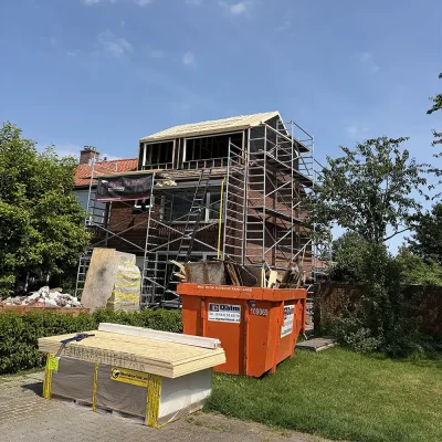 Woning in aanbouw met steigers en een afvalcontainer tijdens de nokverhoging