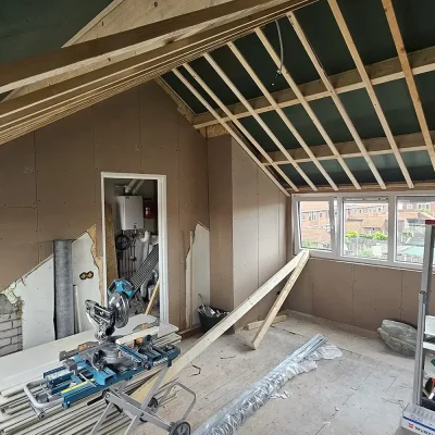 Kamer in aanbouw onder de nieuwe kapconstructie, met een verwarmingsketel en bouwmaterialen