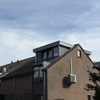 Zijaanzicht van een prefab dakkapel met antracietkleurige gevelbekleding op een bakstenen woning